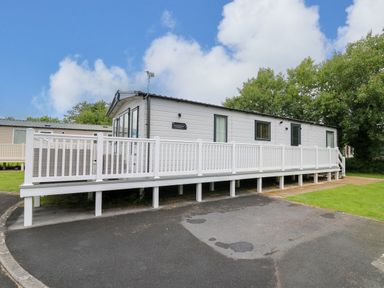 A white mobile home with a long white porch railing on a paved area and grass at Osprey 6 in Kiln Park Tenby