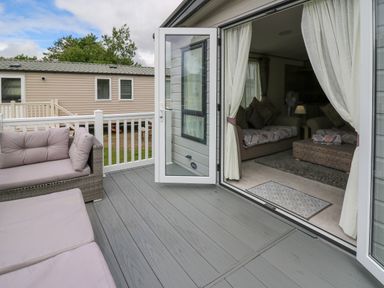 A patio with outdoor seating and an open door leading into a living room at Osprey 6 in Kiln Park Tenby