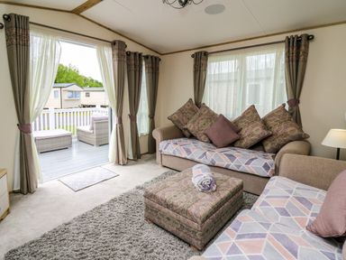 A living room with two sofas a pouf and curtains opened to a patio at Osprey 6 Kiln Park Tenby