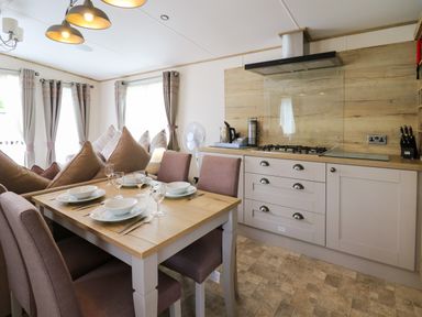 A dining area with a wooden table set with bowls and glasses next to a kitchen with stove and cabinets at Osprey 6 in Kiln Park Tenby