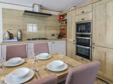 A kitchen with dining table set for four and wooden cabinetry with built in oven and microwave at Osprey 6 in Kiln Park Tenby