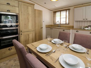 A kitchen with a dining table set with plates and glasses at Osprey 6 Kiln Park Tenby