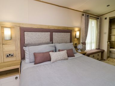 A bedroom with a bed pillows nightstands and a window with curtains at Osprey 6 Kiln Park Tenby
