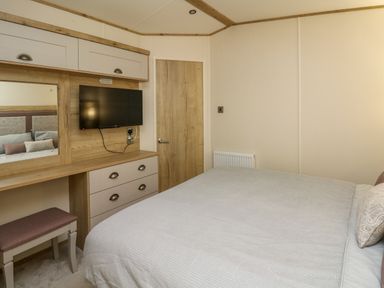 A bedroom with a bed a wall mounted tv a wooden door and a dressing table with stool at Osprey 6 in Kiln Park Tenby