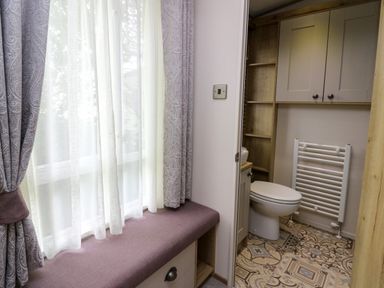 A bathroom with a toilet and radiator next to a seating area by a window at Osprey 6 Kiln Park Tenby
