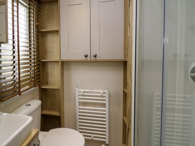 A bathroom with a toilet sink cabinet wall shelves radiator and a shower enclosure at Osprey 6 Kiln Park Tenby