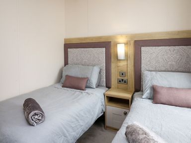 A bedroom with two single beds separated by a wooden nightstand with a lamp on the wall at Osprey 6 Kiln Park Tenby