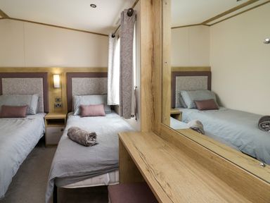 A bedroom with two single beds a bedside table and a wooden dressing table with a mirror at Osprey 6 Kiln Park Tenby