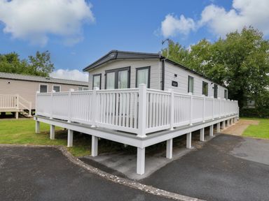 A static caravan with white railings on an elevated deck in a park setting at Osprey 6 Kiln Park Tenby