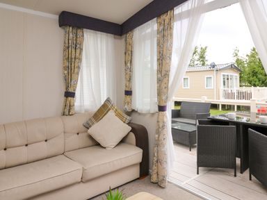 A living room with a beige sofa and patterned curtains next to an outdoor patio with black wicker furniture at Osprey 7 in Tenby
