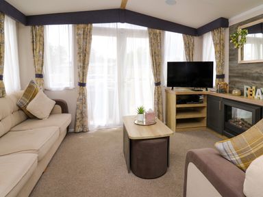 A living room with beige sofa plaid cushions wooden coffee table tv and fireplace at Osprey 7 in Tenby