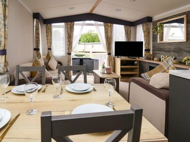 A dining table with plates and glassware in a living room with couches a television and large windows at Osprey 7 in Tenby