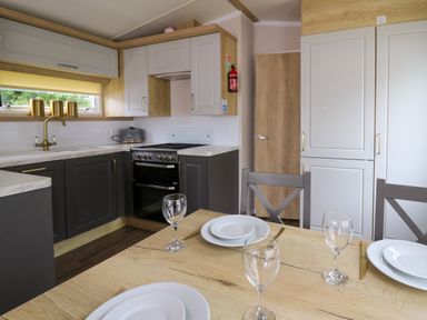 A kitchen with a wooden dining table set with plates and glasses and grey and white cabinets at Osprey 7 in Tenby
