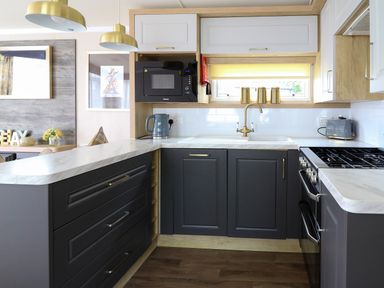 A kitchen with dark and white cabinets a microwave kettle toaster stovetop and sink at Osprey 7 in Tenby