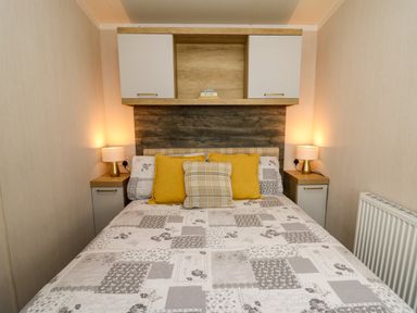 A bedroom with a bed with patterned bedspread yellow pillows wooden cabinets and bedside tables with lamps at Osprey 7 in Tenby