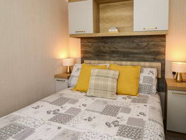 A bedroom with patterned bedspread yellow pillows bedside tables and lamps at Osprey 7 in Tenby