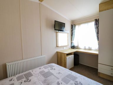 A bedroom with a bed a wall-mounted TV a corner desk near a window with curtains and a wardrobe at Osprey 7 in Tenby
