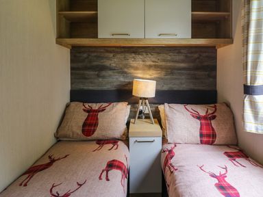 A bedroom with two single beds with deer patterned bedding and a bedside table with a lamp at Osprey 7 in Tenby