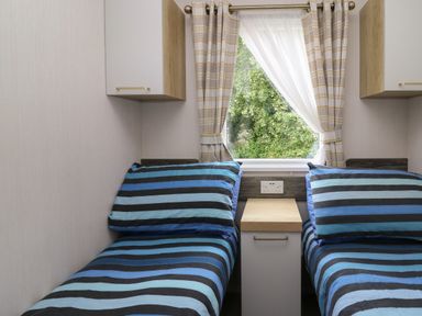 A bedroom with two single beds striped bedding nightstand between beds and a window with curtains at Osprey 7 in Tenby