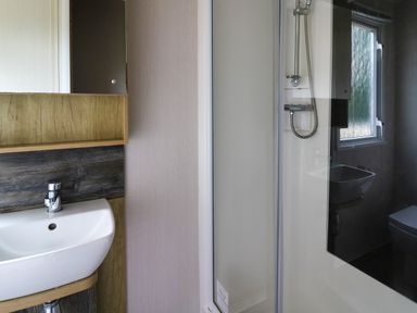A bathroom with a white sink and faucet next to a shower enclosure with a window in the background at Osprey 7 in Tenby