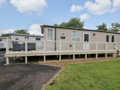 A beige mobile home with a raised deck and outdoor seating in a park setting at Osprey 7 in Tenby