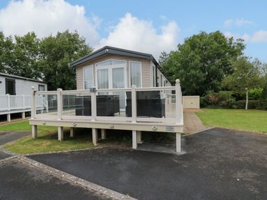 A mobile home with a deck and outdoor seating on a paved area with grass and trees at Osprey 7 in Tenby