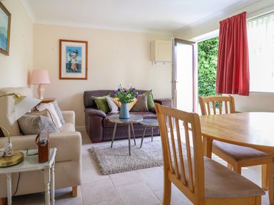 A living room with sofas a coffee table with flowers a wooden dining table and chairs and an open door at Seaweed Weston near Sidmouth
