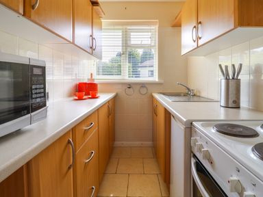 A narrow kitchen with wooden cabinets a microwave a sink an electric stove and orange cups at Seaweed Weston near Sidmouth