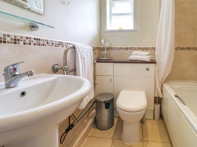 A bathroom with a sink, towel rack, toilet, trash bin, countertop with folded towels, small mirror, and bathtub at Seaweed in Weston near Sidmouth