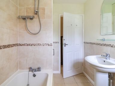 A bathroom with a bathtub with shower, a sink, and a partially open door at Seaweed Weston near Sidmouth