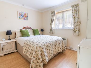 A bedroom with a double bed with floral bedding two green pillows two bedside tables with black lamps and a window with floral curtains at Seaweed Weston near Sidmouth