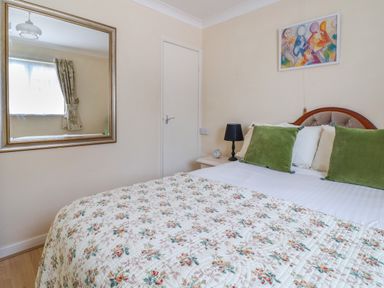 A bedroom with a bed with floral quilt and green pillows a bedside table with a lamp and clock a wall mirror and an abstract painting at Seaweed Weston near Sidmouth