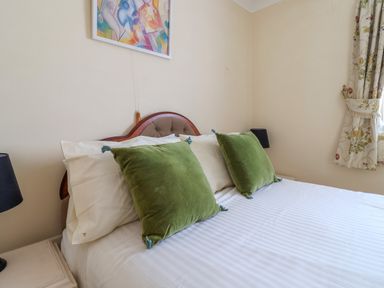 A bedroom with a bed with green pillows white sheets bedside tables with lamps and floral curtains at Seaweed Weston near Sidmouth