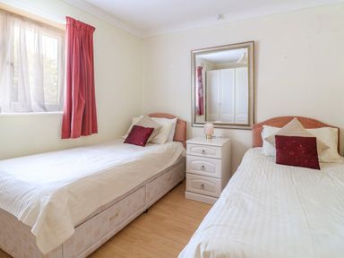 A bedroom with two single beds a nightstand between them and a window with red curtains at Seaweed Weston near Sidmouth