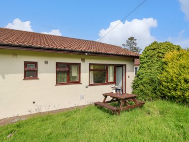 A side view of a beige house with brown framed windows and a wooden picnic table on grass at Seaweed Weston near Sidmouth