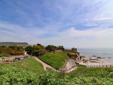 A coastal scene with green hills a pathway a building near the shore and the sea at Seaweed Weston near Sidmouth