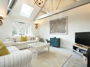 A living room with striped sofas yellow cushions a wooden coffee table a blue cabinet a television and exposed ceiling beams at East Farm Croft in Embleton