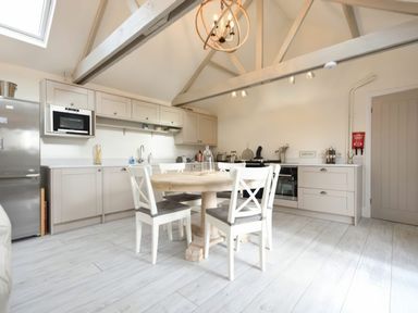 A kitchen with a round wooden table and four chairs under a vaulted ceiling with exposed beams at East Farm Croft in Embleton
