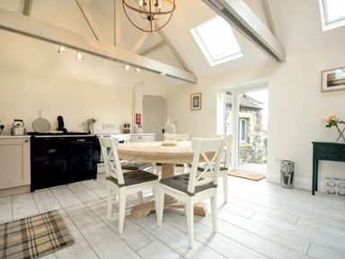 A kitchen with a round wooden dining table and four chairs a black stove white cabinets skylights and a door leading outside at East Farm Croft in Embleton