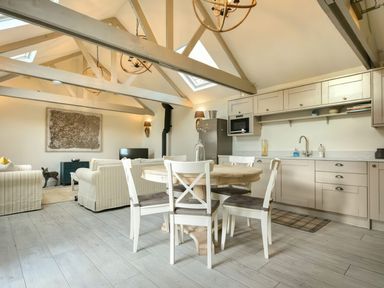 An open kitchen and living area with a round wooden dining table and four white chairs at East Farm Croft in Embleton