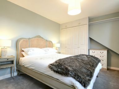 A bedroom with a bed with a fur throw two bedside tables with lamps a chest of drawers and built in wardrobes at East Farm Croft in Embleton