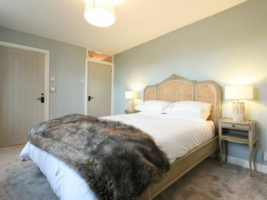 A bedroom with a bed with a woven headboard and fur throw with two bedside tables and lamps at East Farm Croft in Embleton