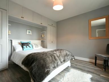 A bedroom with a bed covered in white and gray blankets and cushions a mirror on the wall and a chair at East Farm Croft Embleton