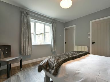 A bedroom with a bed covered with a fur throw a chair near a window and two doors at East Farm Croft in Embleton