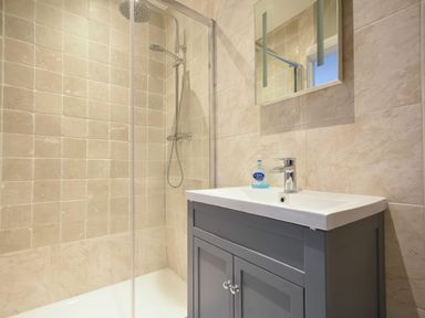 A bathroom with a shower enclosed by glass and a sink with cabinet and mirror at East Farm Croft in Embleton