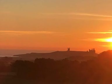 A sunset view over a landscape with trees and distant castle ruins at East Farm Croft in Embleton