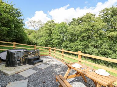 An outdoor area with a hot tub gravel ground and a wooden picnic table set with plates and glasses at Shepherd's Cwtch in Cilycwm near Llandovery