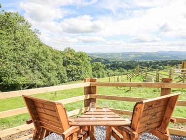 A wooden table and two chairs on a patio overlooking a grassy field and distant hills at Shepherd's Cwtch Cilycwm near Llandovery
