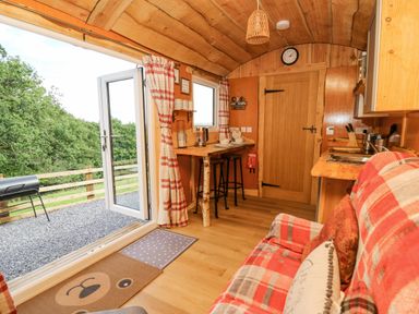 A small wooden kitchen and dining area with stools a plaid sofa and open glass door leading outside at Shepherd's Cwtch in Cilycwm near Llandovery