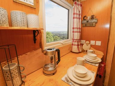 A kitchen counter with cups plates and bowls next to a window with a countryside view at Shepherd's Cwtch in Cilycwm near Llandovery